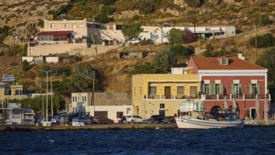 Buildings and boats along the coastline with hills in the background in sunny weather, Agia Marina,