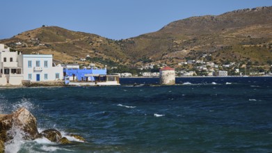 View of a coastal landscape with windmill, blue water and houses in front of hills, Agia Marina,