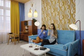 Two friends are seated on a vibrant blue sofa in a stylish living room filled with natural light