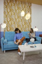 Friends spend a pleasant afternoon in a modern lounge, sitting on a turquoise sofa. They engage in