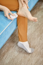 Unrecognizable woman use electric gadget to peel her heel from rough or dead skin while sitting on