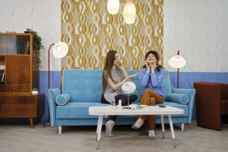 In a stylish living room, two women share a joyful moment while taking care of the skin of their