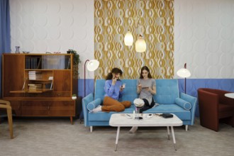 Two friends are seated on a vibrant blue couch in a modern living room, engaged in light