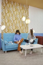 Two young women are engaged in skin care procedures at home sitting on a cozy sofa. One woman rubs