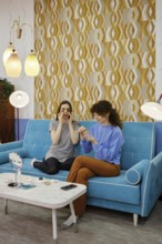 Two friends are enjoying a relaxed moment on a blue couch, engaged in a beauty session. They are