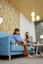 A woman is enjoying a pedicure while seated on a vibrant blue couch at home and chatting with her