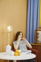 Young woman relaxing in a cozy living room with tea and fruit, surrounded by warm decor and soft