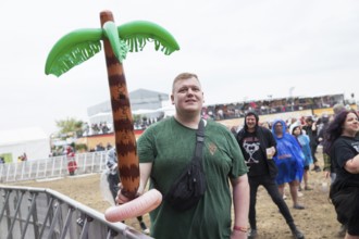 A festival visitor stands with an inflatable palm tree in the rain at the Highfield Festival on
