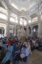 Indian woman pray between the white marble pillars around a marble elephant statue in the Adinath