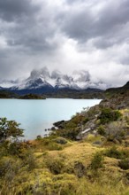 Cloudy mountain range Cuernos del Paine, shore of the blue lake Lago Pehoe in the evening light,