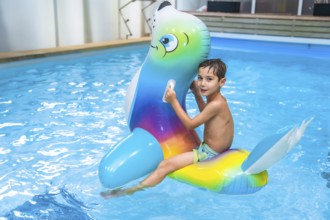 Boy enjoying summer holidays while riding an inflatable toy in a vibrant blue swimming pool,