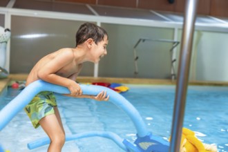 Happy boy playing with a pool noodle in an indoor swimming pool, relishing a fun summer activity
