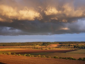 Field landscape in autumn, ploughed fields under dark storm clouds with rainbow in the evening