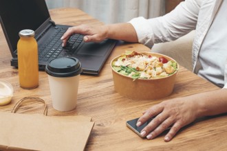 A woman is working on a laptop at home, there is food on the table, salad, coffee and juice,