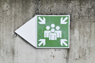 Emergency assembly point sign on concrete wall. Indicates designated safe meeting area for