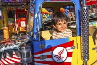 Young boy with a joyful expression sitting in a colorful amusement park ride, surrounded by bright