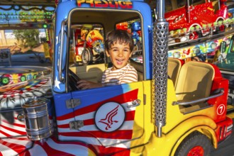 Smiling child enjoying a vibrant amusement park ride, sitting in a brightly colored truck,