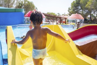 Young boy climbing up a vibrant yellow waterslide at a lively water park, embracing the joy of