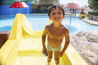 Smiling boy holding a toy car, enjoying summer vacation while sliding down a bright yellow