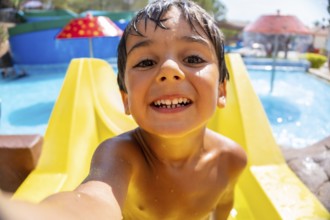 Smiling boy taking a selfie while having fun on a waterslide at a water park during summer vacation