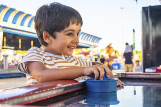 Smiling young boy playing a game at an amusement park, surrounded by colorful attractions and
