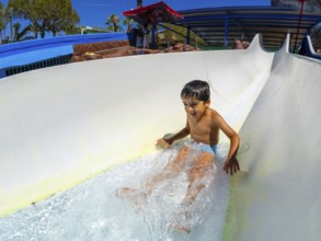 Excited boy sliding down a waterslide at an amusement park, reveling in the joy of summer vacation