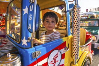 Young boy driving a vibrant, colorful toy truck while enjoying a playful day at a funfair carousel,