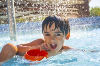 Portrait of a smiling child playing with an orange plastic bucket in a swimming pool under water