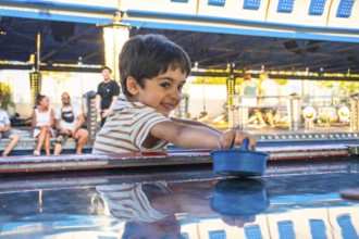 Smiling boy playing air hockey at an amusement park, surrounded by colorful lights and people,