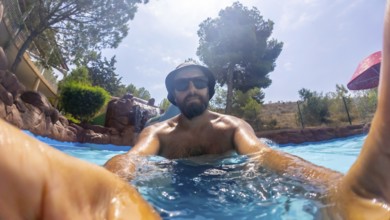 Bearded man wearing bucket hat and sunglasses enjoys relaxing in a water park pool on a sunny day,