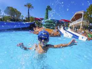 Happy child wearing blue baseball cap and swimming goggles, playing and splashing in a pool during
