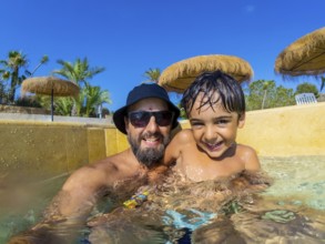 Happy father and son are spending quality time together, playing in swimming pool during summer