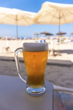 Ice cold beer sitting on a beach bar counter, with white beach umbrellas and ocean in the