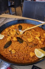Steaming paella with mussels, shrimp, and calamari, served in a traditional pan and garnished with