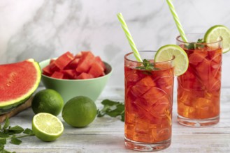 Two glasses with watermelon and lime drink surrounded by ingredients
