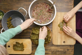 Hands skillfully roll seasoned meat mixture into grape leaves, surrounded by pots and cutting