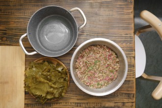 A bowl of prepared ground meat and rice mixture sits next to a plate of grape leaves ready for
