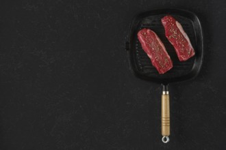 Two raw beef steaks on a preheated griddle pan, seasoned with spices, in a home kitchen setting.
