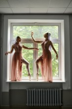 Two ballerinas in transparent long dresses dancing on the windowsill in the corridor