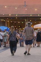 A couple holding hands and walking through a lively evening event, 950 years Weil der Stadt