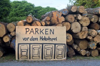 Parking regulations for cars, handwritten and hand-drawn parking sign in front of a woodpile,