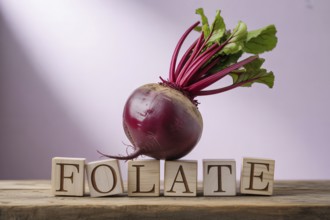 Beetroot with wooden blocks spelling Folate against a pastel violet studio background. Clean