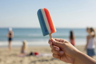 Hand holding melting American flag colored popsicle on sunny beach symbolizing summer and patriotic