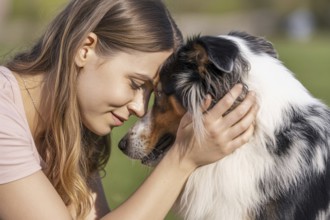 Woman holding Australian Shepherd dog with foreheads touching. Tender moment of emotional