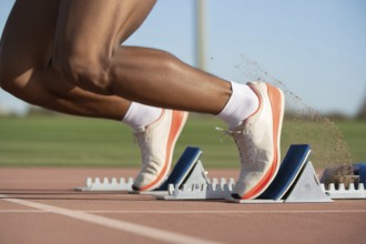 Close-up of athlete in running shoes on starting block at running track. Concept of speed and