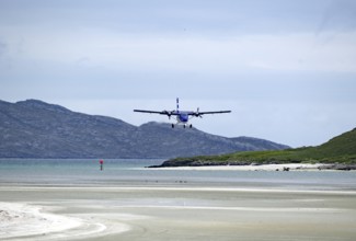 An aeroplane lands on a runway on the beach with mountains in the background and a calm atmosphere,