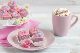 Pink petit fours and a cup of coffee with cream on a table