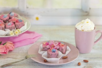 Pink petit fours and a cup of coffee and cream on a table