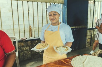Portrait of a vendor serving and holding two pupusas. Smiling female vendor holding two plates of