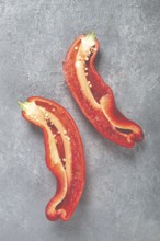 Two halves of vibrant red peppers are displayed on a textured gray surface. The seeds and inner
